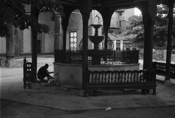 Viaggio in Jugoslavia. Sarajevo: il chiostro della catedrale. Scorcio del luogo - si riconosce un uomo che riempie una brocca di acqua, attingendo alla fontana posta al centro del chiostro