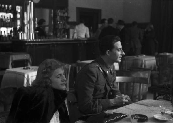 Italia Seconda Guerra Mondiale. Stazione ferroviaria di Riva del Garda: partenza della legione croata. Un gionane soldato seduto con una donna al tavolo del bar-ristoro