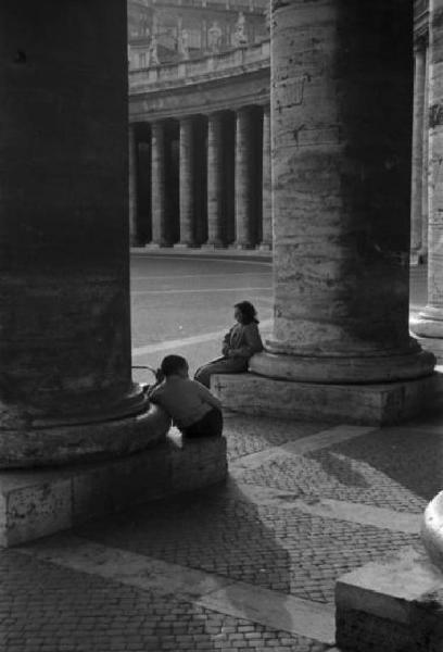 Roma. Piazza San Pietro - colonnato. Una donna e un bambino siedono ai piedi delle colonne