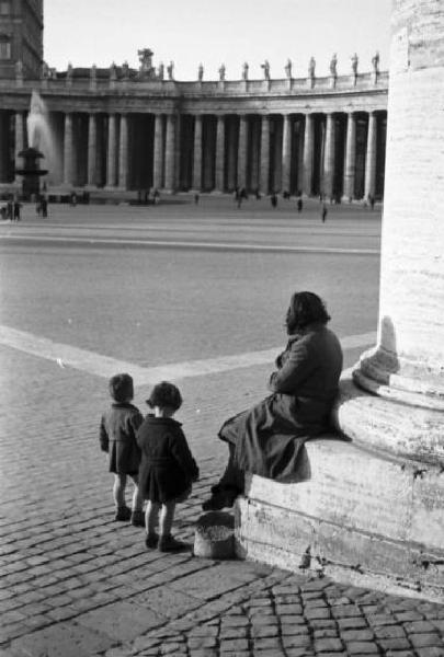 Roma. Scorcio di Piazza San Pietro. In primo piano coppia di bambine con donna seduta ai piedi di una colonna