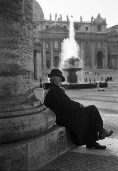 Roma. Scorcio di  Piazza San Pietro. In primo piano un uomo anziano siede ai piedi di una colonna. Sullo sfondo una delle fontane della piazza