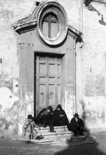 Roma. Alcuni uomini anziani chiacchierano seduti davanti al portone di una chiesa