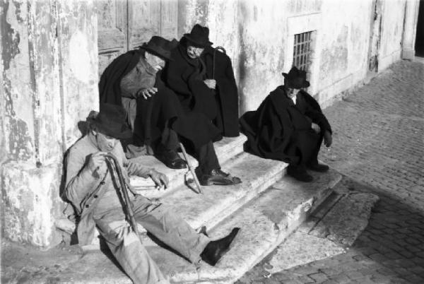 Roma. Alcuni uomini anziani chiacchierano seduti davanti al portone di una chiesa