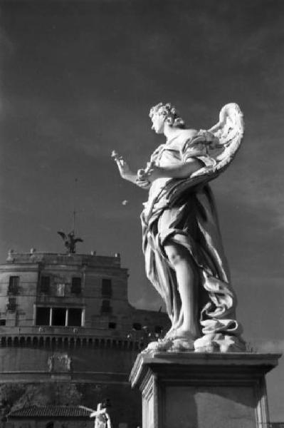 Roma. Ponte Sant'Angelo - una delle dieci statue di angeli che decorano le spallette del ponte. Sullo sfondo è visibile in parte il castello in origine mausoleo