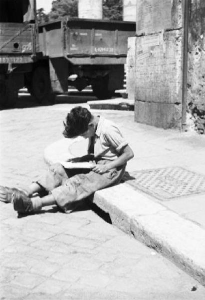 Roma - Bambino legge seduto sul marciapiede
