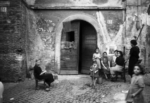 Italia Dopoguerra. Roma - Quartiere Trastevere - Scorcio di un cortile urbano con gruppo di famiglia davanti alla soglia di casa