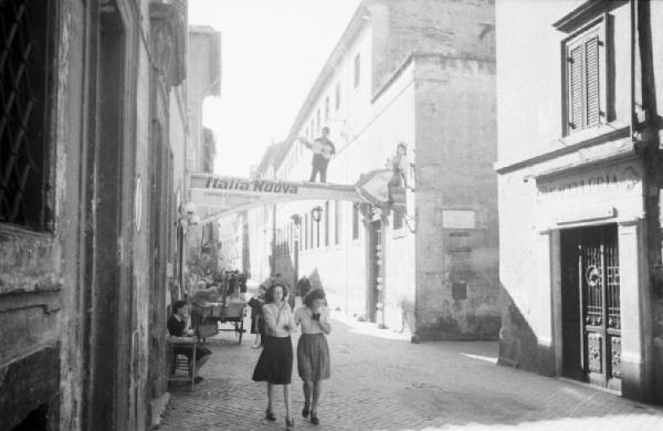 Italia Dopoguerra. Roma - Quartiere Trastevere - via affiancata da bassi edifici - coppia di giovani ragazze cammina per strada