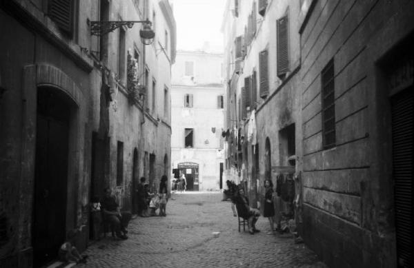 Italia Dopoguerra. Roma - Quartiere Trastevere - Scorcio di una strada con gruppi di persone davanti ai portoni di casa