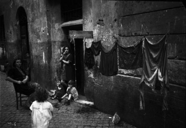 Italia Dopoguerra. Roma - Quartiere Trastevere - gruppo famigliare sulla soglia di casa - panni stesi lungo la facciata