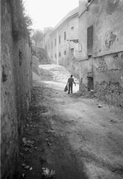 Italia Dopoguerra. Roma - Quartiere Trastevere - via in terra battuta fiancheggiata da edifici - uomo