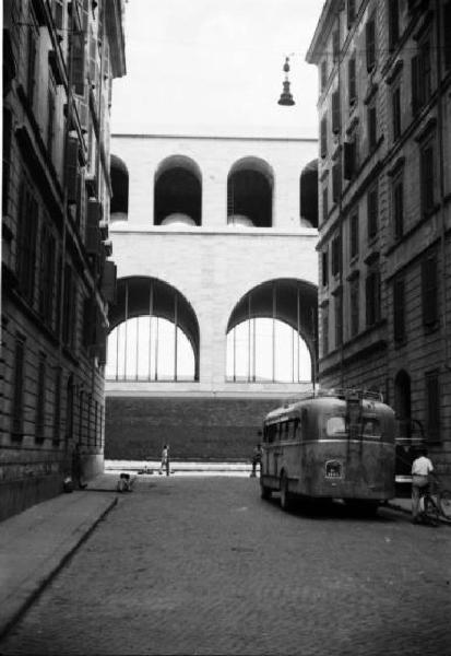 Italia Dopoguerra. Roma - stretta via fiancheggiata da palazzi - corriera - edificio porticato