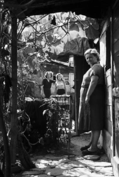 Italia Dopoguerra. Milano - Periferia - Baraccopoli - Ritratto di gruppo sotto un pergolato, donne in posa tra le baracche
