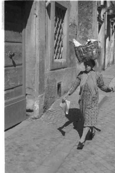 Castel Gandolfo. Scene di vita quotidiana - una donna cammina lungo una strada portando una cesta appoggiata sulla testa