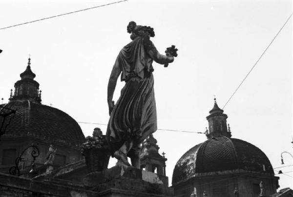 Roma. Piazza del Popolo - statua del gruppo scultoreo sotto il Pincio si staglia contro le cupole delle chiese gemelle di Santa Maria di Montesanto e Santa Maria dei Miracoli