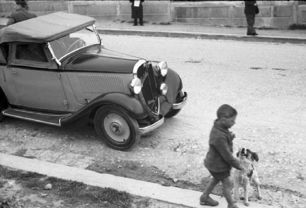 Palermo. Automobile decapottabile Balilla a bordo marciapiede. In primo piano bambino con cane