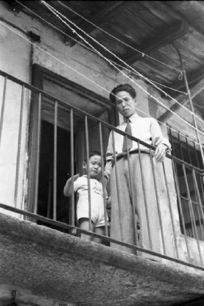 Italia Dopoguerra. Milano - Quartiere cinese - un uomo cinese sul ballatoio di una casa a ringhiera tiene per mano un bambino