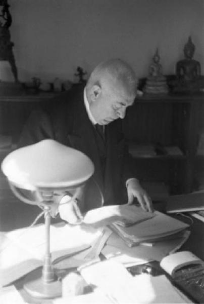 Roma. Francesco Nitti al tavolo del suo studio - quaderni, fogli sparsi e lampada da tavolo - sullo sfondo alcune statuine orientali