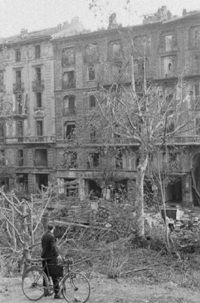 Italia Seconda Guerra Mondiale. Milano. La città dopo il bombardamento del 12 agosto 1943, edifici danneggiati, macerie e alberi abbattuti sotto lo sguardo di un uomo in bicicletta