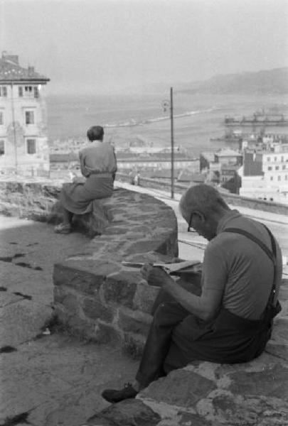 Italia Dopoguerra. Trieste - Anziano legge il giornale seduto su un muretto panoramico che affaccia sulla città e sul golfo