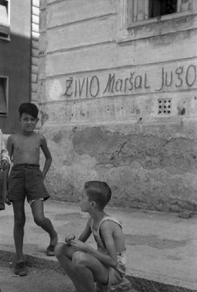 Italia Dopoguerra. Trieste - Ragazzini per strada nei pressi di un muro ricoperto di scritte di sapore politico inneggianti alla Jugoslavia [?]