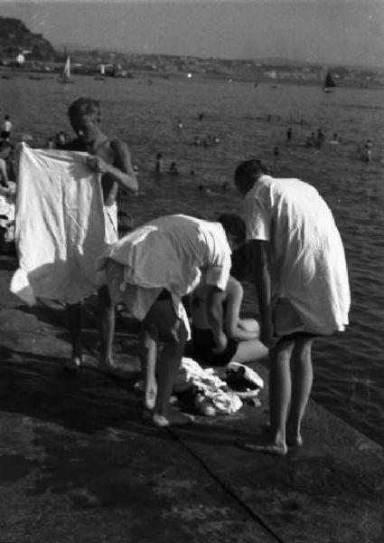 Italia Dopoguerra. Trieste. Lungomare verso Miramare, giovani bagnanti che si cambiano coprendosi con gli asciugamani