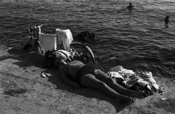 Italia Dopoguerra. Trieste. Lungomare verso Miramare, bagnante che prende il sole sdraiata sul cemento