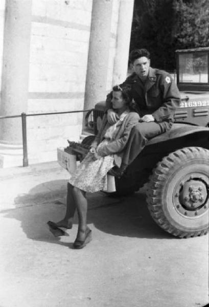 Pisa. Campo dei Miracoli. Militare e ragazza seduti sul parafango di una jeep militare sotto la torre pendente