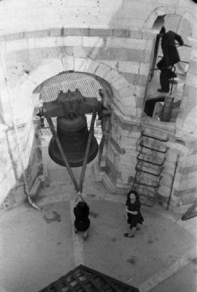 Pisa. Due giovani donne sulla cima della torre pendente - una di esse è aggrappata alle chinghie per suonare la campana - un uomo sale per la scala a muro laterale