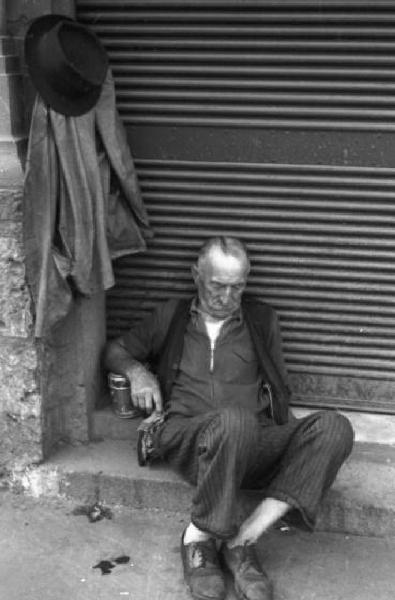 Italia Dopoguerra. Milano - Un uomo anziano dorme seduto davanti alla serranda abbassata di un negozio