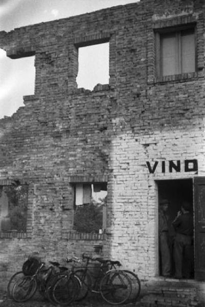 Italia Dopoguerra. Marzabotto - Un edificio semidistrutto con rivendita di vino - Lungo il muro esterno sono appoggiate delle biciclette