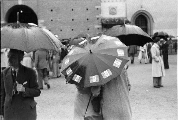 Referendum 1946 Repubblica o Monarchia. Milano - Piazza del Cannone - Manifestazione monarchica - Coppia con ombrello con adesivi della bandiera monarchica