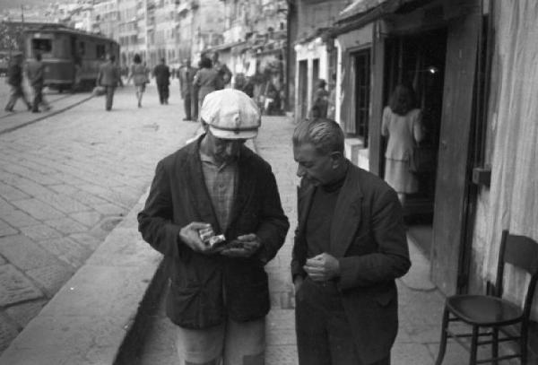 Italia Dopoguerra. Genova - Momenti di vita quotidiana - coppia di uomini chiacchiera lungo una strada della città