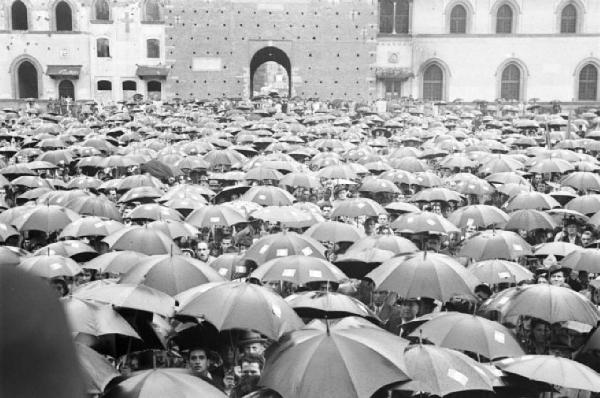 Referendum 1946 Repubblica o Monarchia. Milano - Piazza del Cannone - Manifestazione monarchica - Folla riparata sotto ombrelli con adesivi della bandiera monarchica - sullo sfondo il muro perimatrale interno del Castello Sforzesco