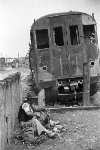 Italia Dopoguerra. Marzabotto - Abitante del paese seduto nei pressi di un vagone ferroviario distrutto dai bombardamenti