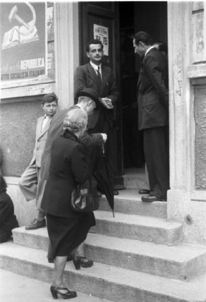 Referendum 1946 Repubblica o Monarchia. Milano - Ufficio elettorale - Coppia di anziani - Sul muro manifesto del Partito Socialista Italiano