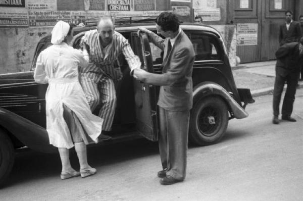 Referendum 1946 Repubblica o Monarchia. Milano - Ufficio elettorale - Infermiera e uomo adulto aiutano anziano a scendere dall'automobile
