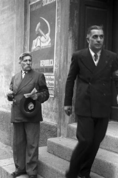 Referendum 1946 Repubblica o Monarchia. Milano - Ufficio elettorale - Due cittadini - Sul muro manifesto del Partito Socialista Italiano