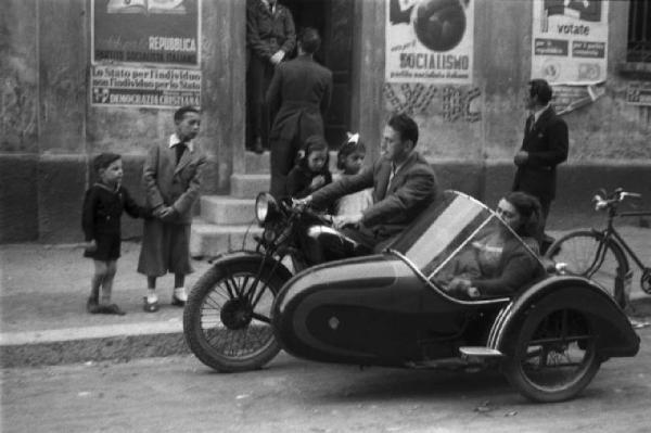 Referendum 1946 Repubblica o Monarchia. Milano - Ufficio elettorale - Coppia sul side-car - Bambini - Sul muro manifesti elettorali e scritte