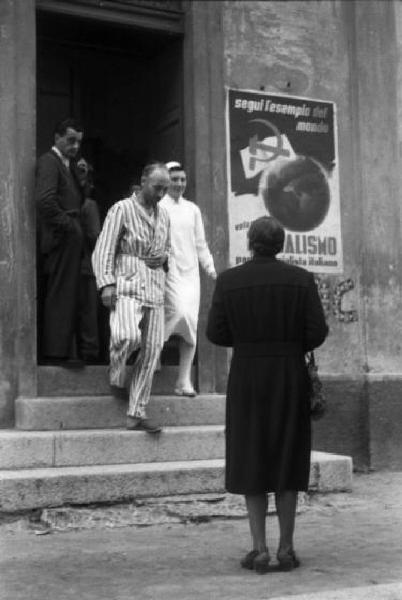 Referendum 1946 Repubblica o Monarchia. Milano - Ufficio elettorale - Infermiera aiuta un anziano - Sul muro manifesto del Partito Socialista Italiano