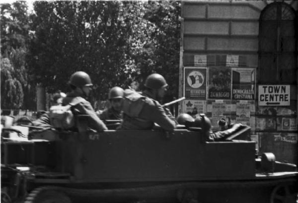 Italia Dopoguerra. Milano. Mezzo militare cingolato con soldati di passaggio presso l'Arco della Pace - sullo sfondo insegne stradali in lingua inglese