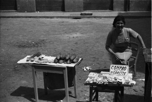 Italia Dopoguerra. Roma - Quartiere Trastevere - Mercato nero [?] - Donna seduta per strada che acquista sigarette