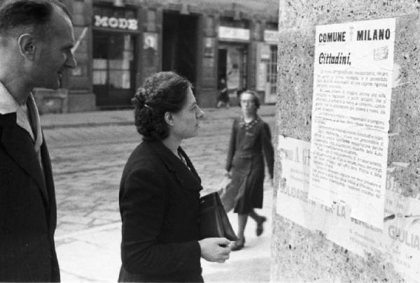 Italia Dopoguerra. Milano. Vendita di prodotti a prezzi calmierati. Uomo e donna leggono un manifesto con un'ordinanza del Comune di Milano