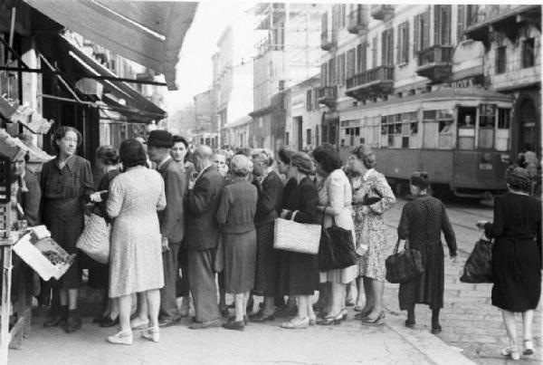 Italia Dopoguerra. Milano. Vendita al mercato di prodotti a prezzi calmierati. Coda di persone davanti a un fruttivendolo