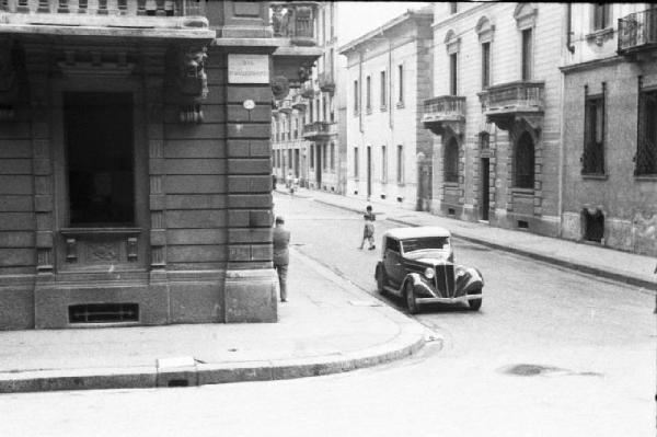 Italia Dopoguerra. Milano. Vendita al mercato di prodotti a prezzi calmierati. Automobile parcheggiata all'angolo di una via (E.D. Clerrazzi?)