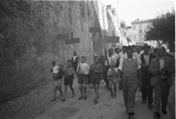 Invasione delle terre. Gruppo di contadini e bambini con cartelli percorrono una strada in discesa