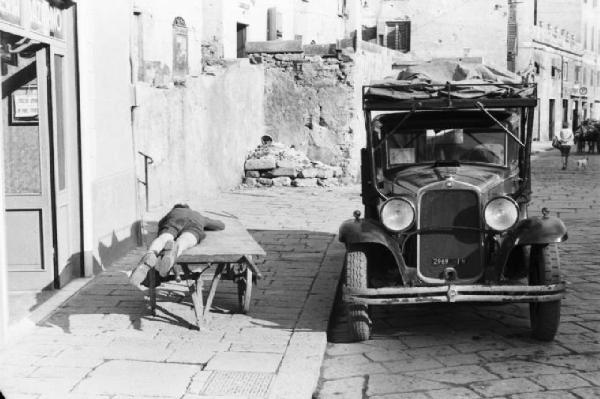 Italia Dopoguerra. Genova - Ragazzo dorme sdraiato su un carretto - automobile parcheggiata