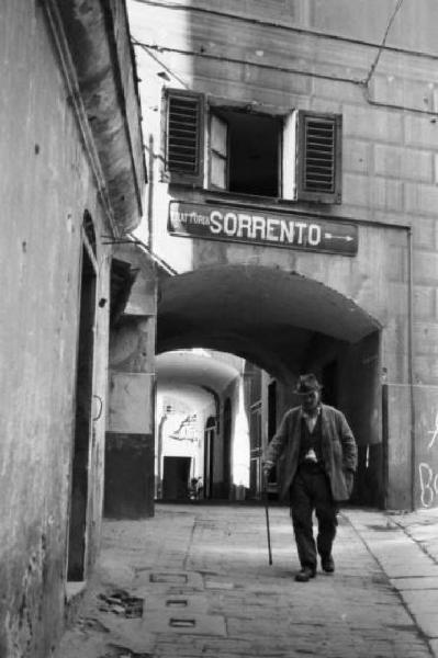 Italia Dopoguerra. Genova - Passaggio porticato - uomo - insegna di trattoria