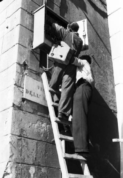 Italia Dopoguerra. Genova - Due tecnici arrampicati su una scala effettuano una riparazione alla linea elettrica di una zona della città