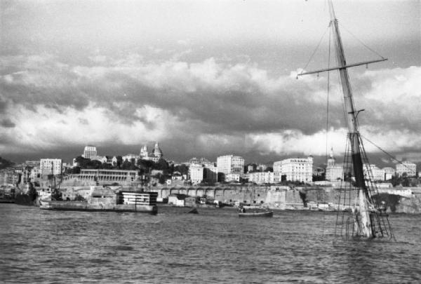 Italia Dopoguerra. Genova - Porto - veduta della costa con relitto di una nave in mare e di cui affiora soltanto l'albero maestro