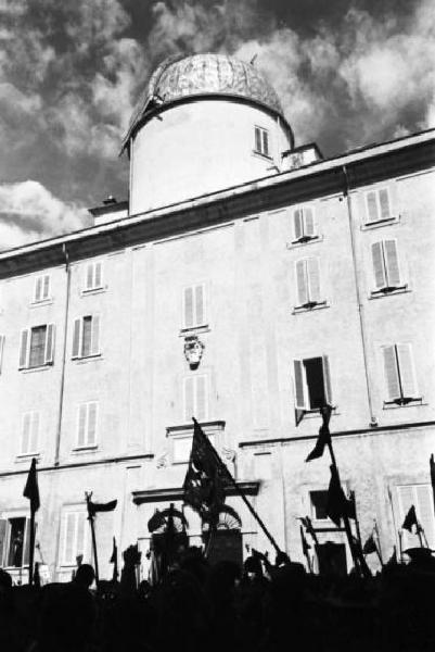 Ike a Castel Gandolfo. Ripresa dal basso di un'ala del Palazzo Vaticano, con una delle cupole in evidenza. In basso spicca la silhouette di una folla di scout con bandiere